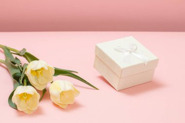 Pembe arka planda sarı laleleri olan beyaz hediye kutusu. Tatillerde hediye verme kavramı.
