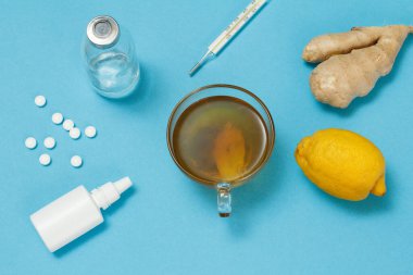 Burun spreyi, haplar, cam şişe, cıva termometre, bir fincan çay, limon ve zencefil. Üst Manzara. Tedavi seti konsepti. Soğuk algınlığı ve grip için sağlıklı besinler.