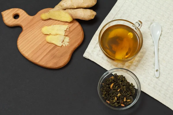 Health remedy foods for cold and flu relief. Cup of tea, ginger and a glass bowl with dried leaves of tea on a black background. Top view. Foods That Boost the Immune System.