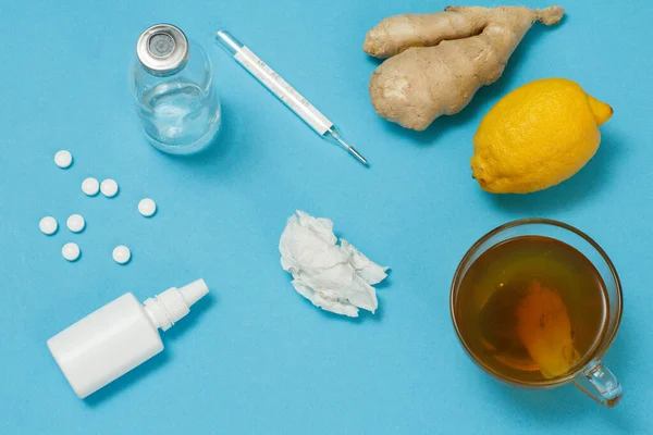 Nasal spray, a used paper napkin, pills, a glass bottlle, a mercury thermometer, a cup of tea, a lemon and a ginger. Top view. Treatment kit concept. Health remedy foods for cold and flu relief.
