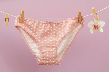 Çamaşır ipinde yeni pembe külotlar, mandallar ve leylak arka planda orkide çiçekleri. Kadın iç çamaşırı.