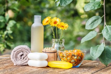 Spa ürünleri ve aksesuarlar. Havlu, sabun ve kadife çiçeği özlü plastik şişe, cam şişede takviye çiçekleri ve eski ahşap tahtaların üzerinde papatya çiçekleri olan tahta kase..