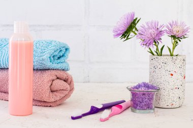 Deniz tuzu, bir şişe şampuan, havlular, diş fırçaları ve beyaz arka planda kasımpatı çiçekleri. Kadın kozmetik ürünleri ve aksesuarları.