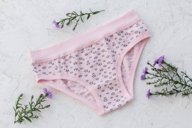 Beyaz yapılı arka planda çiçekler olan pembe pamuklu külotlar. Kadın iç çamaşırı seti. Üst görünüm.
