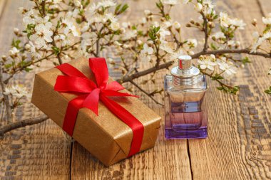 Hediye kutusu ve ahşap zemin üzerinde çiçek açan kiraz ağacı dalları olan bir şişe parfüm. Tatillerde hediye verme kavramı.