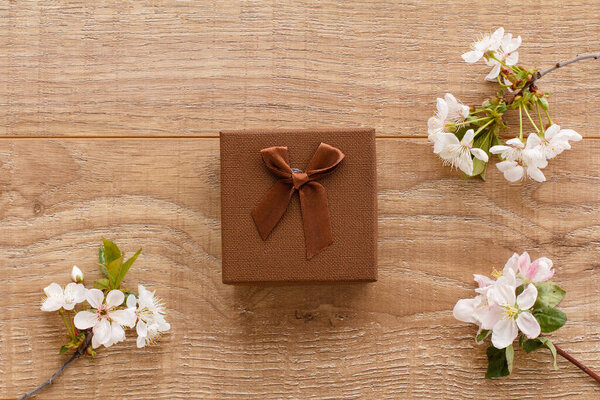 Подарочная коробка с цветущими ветвями вишни и яблони на деревянном фоне. Вид сверху. Концепция дарения подарков в праздничные дни.