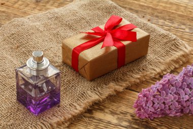 Bir şişe parfüm, bir hediye kutusu ve çuval bezinde leylak çiçekleri ve tahta tahtalar. Tatillerde hediye verme kavramı. Üst görünüm.