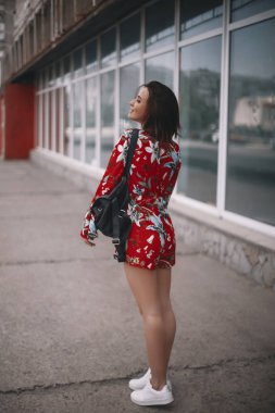 kadın Pencerenin kenarında yürüyor. kısa saçlı, kırmızı tulum tropikal süsleme ile yürüyüş esmer kız.