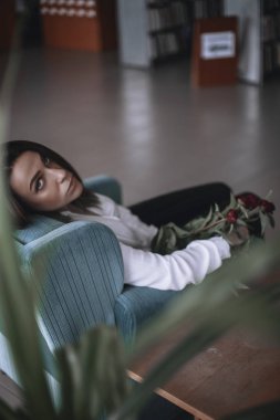 Güzel bir kız bir mavi kadife sandalyede oturan ve istirahat ediyor. Siyah pantolon ve beyaz gömlek bir kadın. kısa saçlı esmer. iş kadını ofiste.