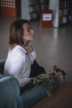 Güzel bir kız bir mavi kadife sandalyede oturan ve istirahat ediyor. Siyah pantolon ve beyaz gömlek bir kadın. kısa saçlı esmer. iş kadını ofiste.