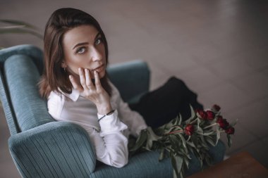 Güzel bir kız bir mavi kadife sandalyede oturan ve istirahat ediyor. Siyah pantolon ve beyaz gömlek bir kadın. kısa saçlı esmer. iş kadını ofiste.