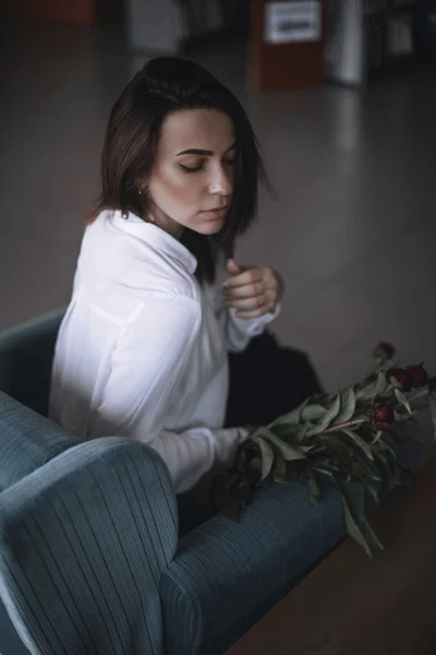 A beautiful girl is sitting on a blue velvet chair and is resting. A woman in black trousers and a white shirt. brunette with short hair. businesswoman in the office. — Stock Photo, Image