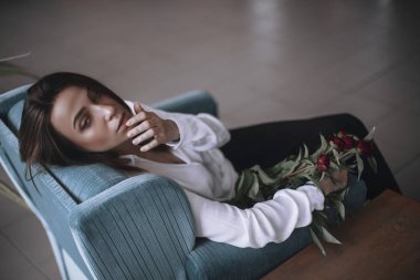 Güzel bir kız bir mavi kadife sandalyede oturan ve istirahat ediyor. Siyah pantolon ve beyaz gömlek bir kadın. kısa saçlı esmer. iş kadını ofiste.