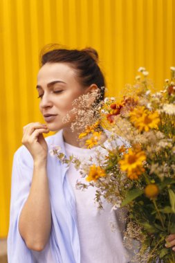 Güzel esmer kadınla sarı arka plan üzerinde topuz kafasındaki alanları çiçekler elinde tutarken mavi gömlek ve beyaz tişört giyiyor. Erkek çiçek getirmek