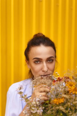 Güzel esmer kadınla sarı arka plan üzerinde topuz kafasındaki alanları çiçekler elinde tutarken mavi gömlek ve beyaz tişört giyiyor. Erkek çiçek getirmek