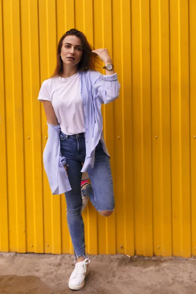 Ganzkörperporträt einer glücklichen schönen Frau, die weißes T-Shirt, blaues Hemd und blaue Jeans trägt und vor gelbem Hintergrund in die Kamera schaut — Stockfoto