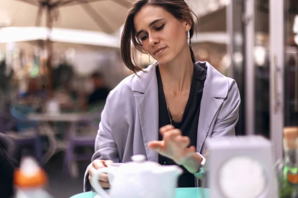 beautiful business woman reaches for a kettle to pour the tea into a cup. attractive girl is resting in a cafe.