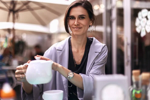 güzel esmer kız bir çaydanlık gelen beyaz bir bardağa çay dökülen. bir kadın bir restoranda dinleniyor. iş kadını kahve molası