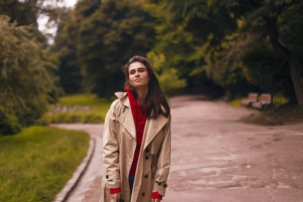 Retrato de mulher vestindo casaco bege, capuz vermelho enquanto caminha no parque. Ela parece feliz. . — Fotografia de Stock