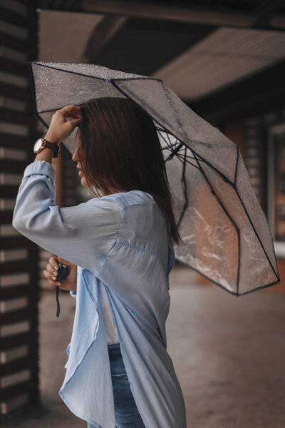 Attractive woman under the umbrella wearing blue shirt. Girl look happy. Rain