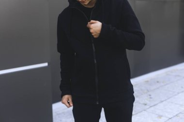 Genç adam onun hoodie sıkıştırma. Adam soyunma siyah spor giyim. Gri kentsel arka plan. 