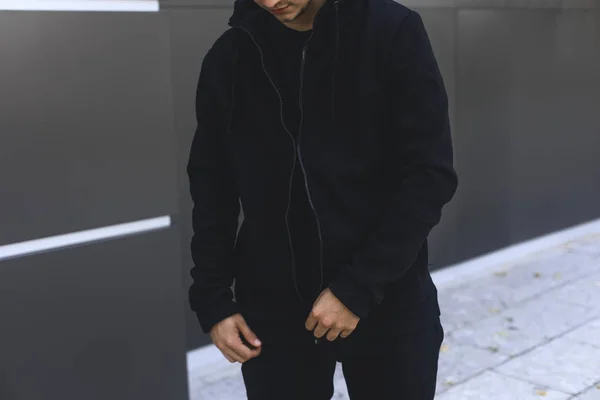 Un jeune homme qui met son sweat à capuche. Homme habillage noir vêtements de sport. Fond urbain gris . — Photo
