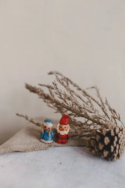 Новый год, Санта-Клаус (Дед Мороз) и Снегурочка, рождественская открытка. Пластиковые фигурки на поверхности текстильного белья. Конус и сухой цветок, как украшение . — стоковое фото