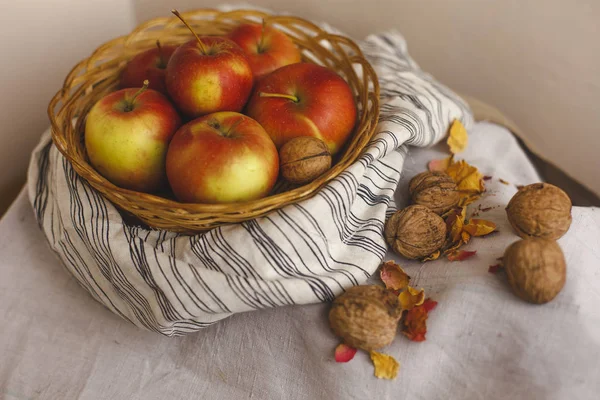 Natürmort bir sepet elma ile stand çizgili bir keten kumaş, ceviz, çiçek yaprakları. Şükran günü kartı oluşturmak için sonbahar ve sonbahar kavramları. Elma fındık ve sonbahar ve sonbahar dekorasyonları.