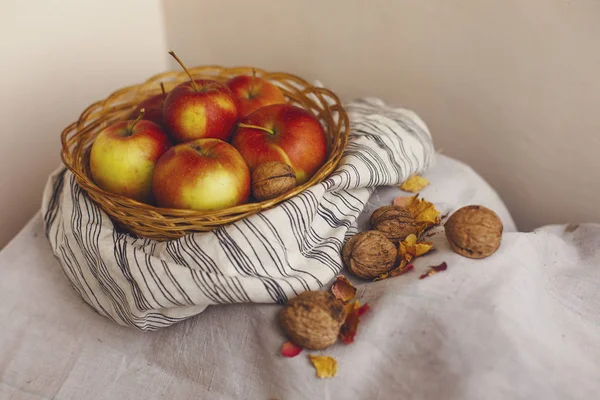 Nature morte avec des pommes dans un panier en osier debout sur un tissu de lin rayé, noix, pétales de fleurs. Création de cartes d'action de grâce pour les concepts d'automne et d'automne. Pommes noix et décorations d'automne et d'automne . — Photo