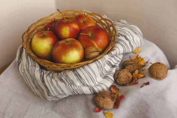 Nature morte avec des pommes dans un panier en osier debout sur un tissu de lin rayé, noix, pétales de fleurs. Création de cartes d'action de grâce pour les concepts d'automne et d'automne. Pommes noix et décorations d'automne et d'automne . — Photo