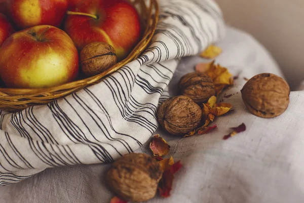 Nature morte avec des pommes dans un panier en osier debout sur un tissu de lin rayé, noix, pétales de fleurs. Création de cartes d'action de grâce pour les concepts d'automne et d'automne. Pommes noix et décorations d'automne et d'automne . — Photo