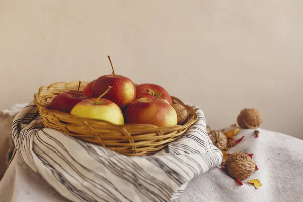 Nature morte avec des pommes dans un panier en osier debout sur un tissu de lin rayé, noix, pétales de fleurs. Création de cartes d'action de grâce pour les concepts d'automne et d'automne. Pommes noix et décorations d'automne et d'automne . — Photo
