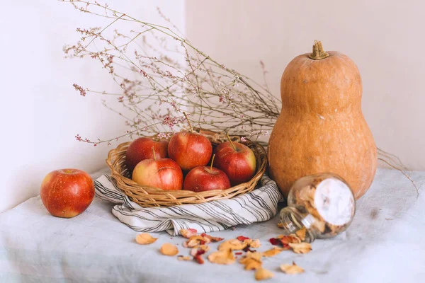 Nature morte avec des bâtons de cannelle enveloppés dans de la ficelle, des pommes dans un panier en osier se tiennent sur un linge rayé, des noix et des pétales de fleurs. Concept de confort à la maison en automne ou en hiver . — Photo