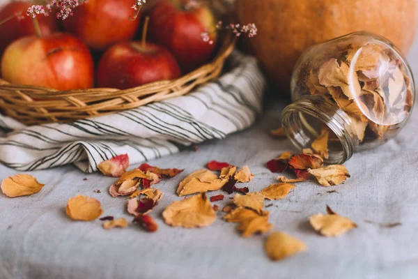 Nature morte avec des bâtons de cannelle enveloppés dans de la ficelle, de la citrouille, des pommes dans un panier en osier sur un chiffon de lin rayé, des noix et des pétales de fleurs en banque. Concept de confort à la maison en automne ou en hiver . — Photo