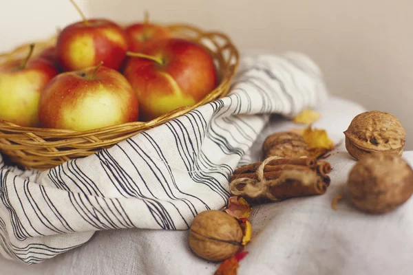 Nature morte avec des pommes dans un panier en osier sur un tissu de lin rayé, noix, pétales de fleurs et bâtons de cannelle enveloppés dans de la ficelle. Création de cartes d'action de grâce pour les concepts d'automne et d'automne . — Photo