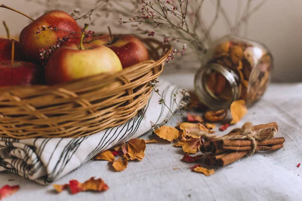 Nature morte avec des bâtons de cannelle enveloppés dans de la ficelle, des pommes dans un panier en osier se tiennent sur un linge rayé, des noix et des pétales de fleurs. Concept de confort à la maison en automne ou en hiver . — Photo