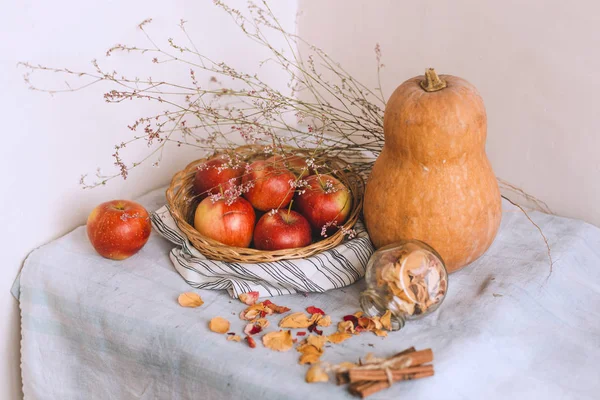 Nature morte avec des bâtons de cannelle enveloppés dans de la ficelle, des pommes dans un panier en osier se tiennent sur un linge rayé, des noix et des pétales de fleurs. Concept de confort à la maison en automne ou en hiver . — Photo