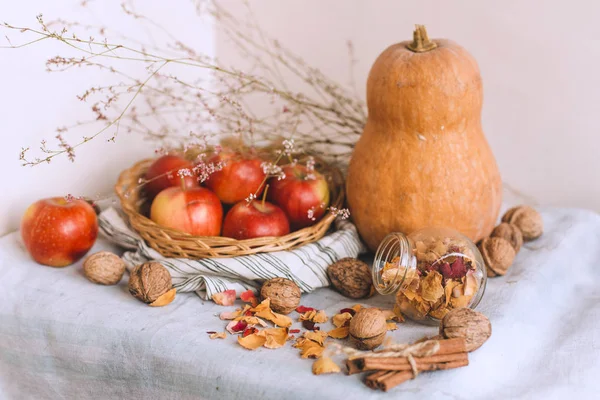 Nature morte avec des bâtons de cannelle enveloppés dans de la ficelle, des pommes dans un panier en osier se tiennent sur un linge rayé, des noix et des pétales de fleurs. Concept de confort à la maison en automne ou en hiver . — Photo