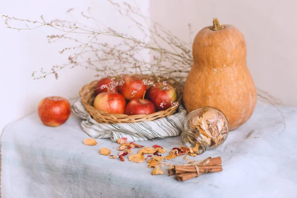 Nature morte avec des bâtons de cannelle enveloppés dans de la ficelle, des pommes dans un panier en osier se tiennent sur un linge rayé, des noix et des pétales de fleurs. Concept de confort à la maison en automne ou en hiver . — Photo