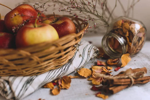 Nature morte avec des bâtons de cannelle enveloppés dans de la ficelle, des pommes dans un panier en osier se tiennent sur un linge rayé, des noix et des pétales de fleurs. Concept de confort à la maison en automne ou en hiver . — Photo