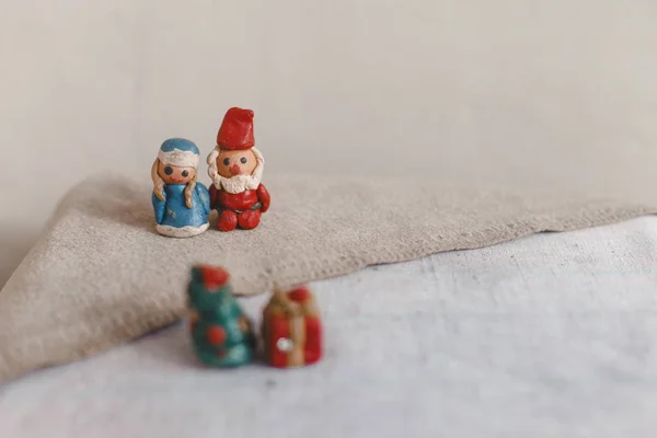 Año Nuevo, Santa Claus (Padre Frost) y Snow Maiden, tarjeta de Navidad. Figuras de plastilina sobre una superficie de lino textil. Primer plano fuera de foco Árbol de Navidad y regalo — Foto de Stock