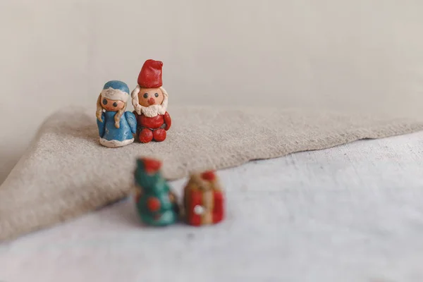 Año Nuevo, Santa Claus (Padre Frost) y Snow Maiden, tarjeta de Navidad. Figuras de plastilina sobre una superficie de lino textil. Primer plano fuera de foco Árbol de Navidad y regalo —  Fotos de Stock