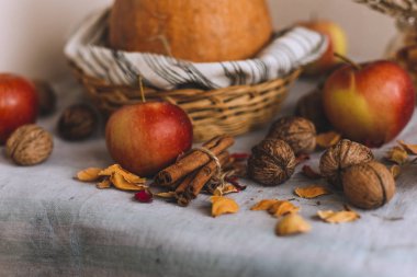 Natürmort tarçın ile sarılmış sicim, elma, çizgili bir keten kumaş, ceviz ve çiçek yaprakları bankada bir hasır sepet stand kabak. Sonbahar ya da kış ev rahatlığında kavramı.