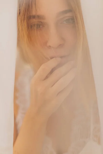 Portrait of young blonde woman under \
white sheet. Bride\'s morning. Woman in white lingerie. Focus on hair. On the photo effect of smokey or mist. Girl is wake up.