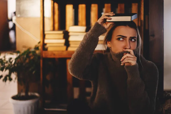 Una donna attraente con un libro in testa. Foto di sguardo femminile bionda scontento modello con emozioni negative, solleva sopracciglia, si sente preoccupato e insoddisfatto . — Foto Stock