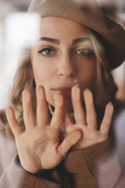 Amazed beautiful female look under the glass window, cover mouth. Woman wears total look. Beige beret. Hand on glass. — Stock Photo, Image