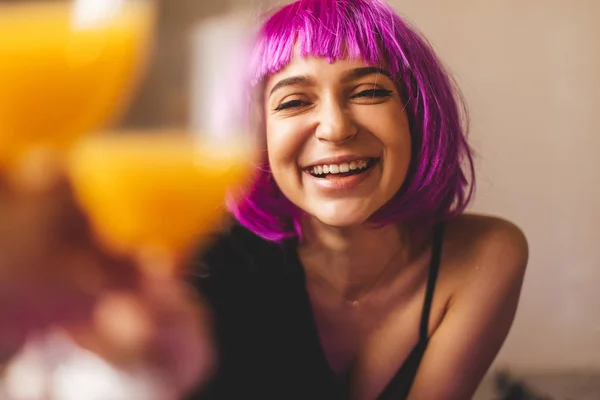 Çekici playfull kadın pembe peruk, siyah iç çamaşırı ve gömlek giyer. Kız bardakta portakal suyu içiyor. Katta oturan kadın. O seksi ve sıcak bak, kız kadeh kaldırdı. Tost