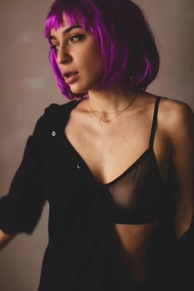 Ελκυστική κοπέλα φορούν ροζ περούκα και μαύρα εσώρουχα, πουκάμισο. Γυναίκες κλείνουν ένα μαύρο πουκάμισο. Σέξι κορίτσι απογειώνεται ή βάζοντας μαύρο πουκάμισο. — Φωτογραφία Αρχείου