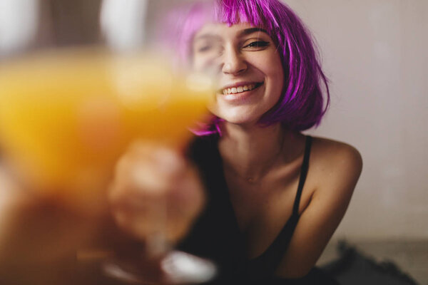 Attractive playfull woman wears pink wig, black lingerie and shirt. Girl drinking orange juice in glass. Woman sitting on the floor. She look sexy and hot, girl raised a glass. Toast — Stock Photo, Image