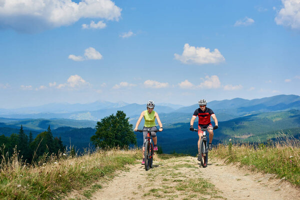 cyclists couple in professional sportswear and helmets on bicycles cycling cross country on  mountain road at bright sunny summer day, Active lifestyle and happy relations concept
